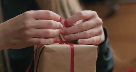 Closeup shot of female hands tying red ribbon bow on craft paper gift box, wide photoの写真素材