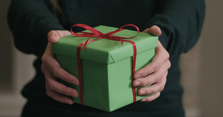 Closeup female hands shows green gift box with red ribbon bow, wide photoの写真素材