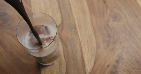 Pour hot cocoa in glass with oat milk on wood background with copy space, wide photoの写真素材