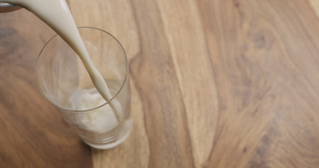 pour oat milk in glass on wood background with copy space, wide photoの写真素材