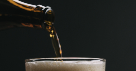 Closeup pour dark beer from brown bottle into glass on black background, wide photoの写真素材