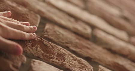 closeup man hand touching old brick wall