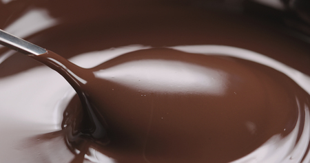 closeup pouring melted dark chocolate from spoonの写真素材