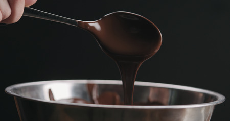 closeup pouring melted dark chocolate from spoon