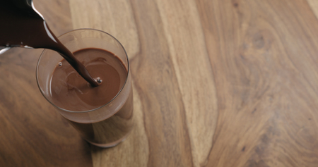 Pour hot cocoa in glass on wood background with copy space, wide photoの写真素材