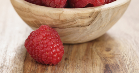 Closeup   of wood bowl full of ripe raspberries on old wooden table