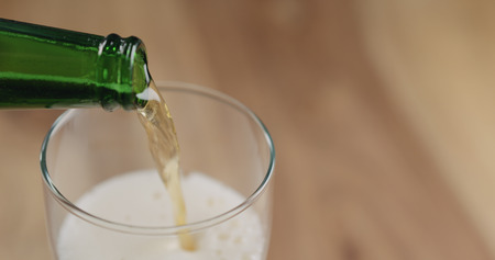 Closeup pour lager beer from green bottle into the glass on wood tableの写真素材