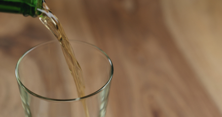 Closeup pour lager beer from green bottle into the glass on wood tableの写真素材