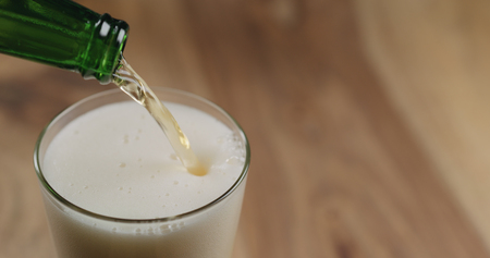 Closeup pour lager beer from green bottle into the glass on wood tableの写真素材