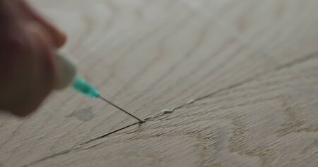 closeup man filling empty spots in wood glue seam with syringe