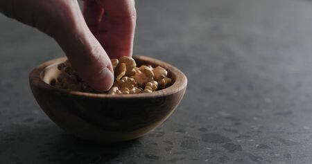 man hand take walnut kernels from wooden bowl on terrazzo countertop