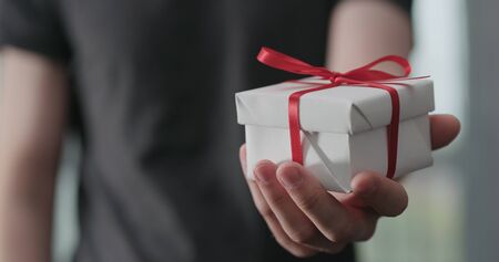 young man shows white paper gift box with red ribbon