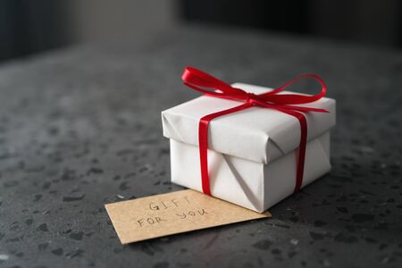 White gift box with red ribbon and paper card on terrazzo surface, shallow focusの写真素材
