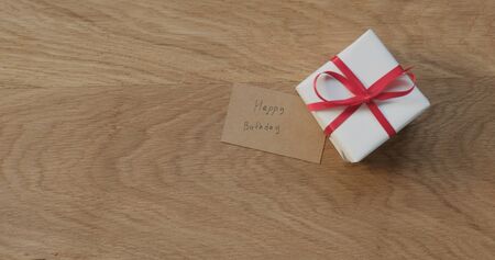 top view gift box with red ribbon and happy birthday card on oak tableの写真素材