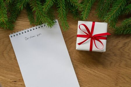 Flat lay christmas gift list notepad with spruce twigs and gift box on oak wood surface, good for backdropの写真素材