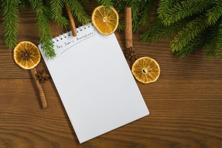 Flat lay new years resolutions notepad with spruce twigs and decorations on ash wood surface good...