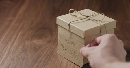 man hand put happy new year card next to brown paper gift box on walnut tableの写真素材