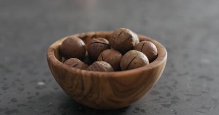 inshell macadamia nuts in olive wood bowl on terrazzo surface