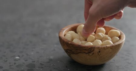 man hand take peeled macadamia nut from olive wood bowl, wide photoの写真素材