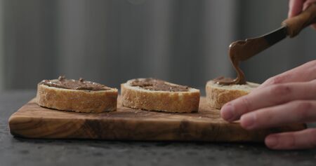 man spreading nut butter on ciabatta slice on olive board