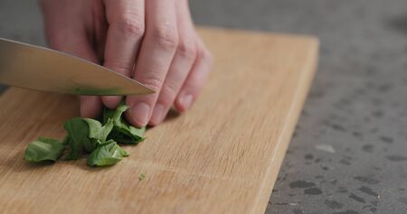man chopping fresh spinach leaves on oak cutting board, wide photo
