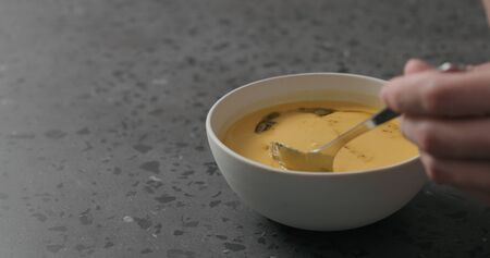 man eating pumpkin cream soup in white bowl on terrazzo countertopの写真素材