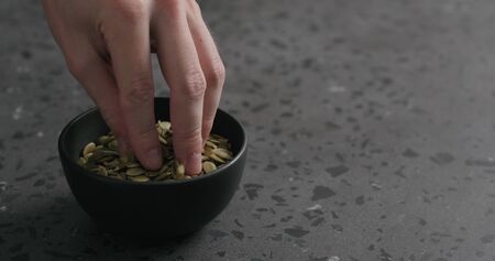 man hand takes pumpkin seeds from black bowl with copy spaceの写真素材