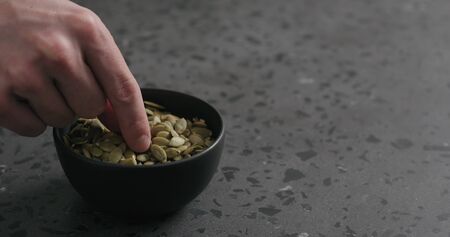 man hand takes pumpkin seeds from black bowl with copy spaceの写真素材