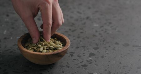 man hand takes pumpkin seeds from olive bowl with copy spaceの写真素材