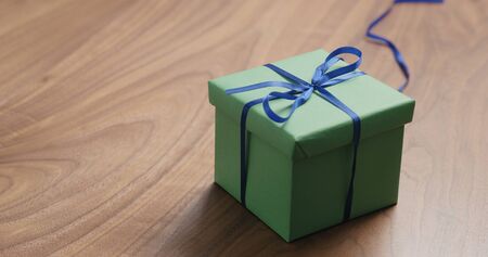 green paper gift box with blue ribbon on walnut table with copy space, wide photoの写真素材
