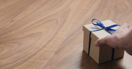 man hand place eco friendly paper gift box with blue ribbon on walnut table with copy space, wide photoの写真素材