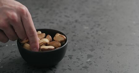 man hand takes brazil nuts from black bowl on terrazzo countertopの写真素材