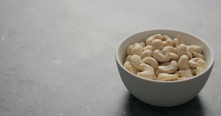 cashew nuts in white bowl on terrazzo countertop, wide photoの写真素材
