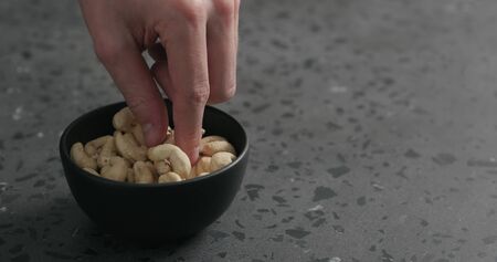 man hand takes cashew nuts from black bowl on terrazzo countertopの写真素材