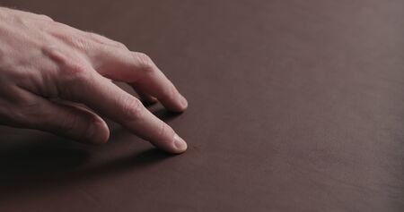 man hand shows scar on brown leather piece closeup, wide photoの写真素材