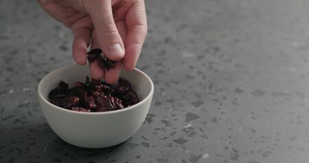 man hand take dried cranberry from white bowl on terrazzo countertop, wide photoの写真素材