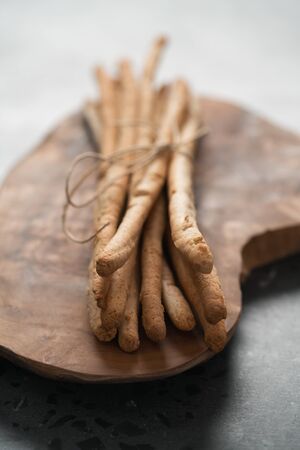 bunch of handmade wholegrain grissini tied with rope on olive board, shallow focus