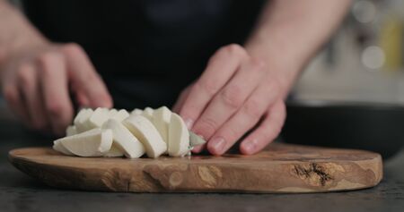 man slicing fresh mozzarella cheese on olive wood board, wide photoの写真素材
