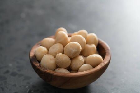 Macadamia nuts in olive wood bowl on terrazzo surface, shallow focusの写真素材