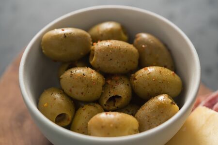 Closeup pitted whole green olives with spices in white bowl, shallow focus