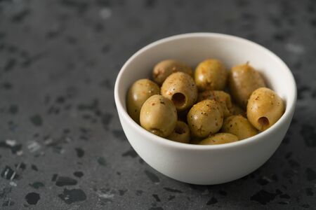 pitted whole green olives with spices in white bowl on terrazzo surface with copy space, shallow focusの写真素材