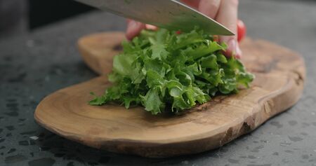 man chopping frisee salad leaves on olive board, wide photoの写真素材