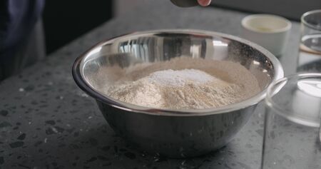 add dry ingredients into flour in steel bowl on concrete countertop