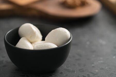 Small mozzarella balls in black bowl on concrete background
