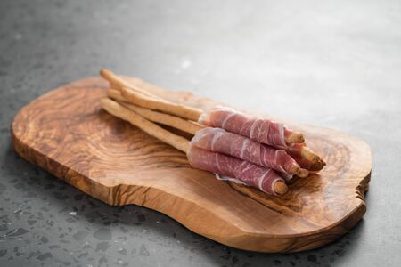 Grissini with prosciutto on olive wood board
