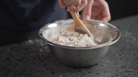 man mixing wet ingredients into flour in steel bowl on concrete countertopの写真素材