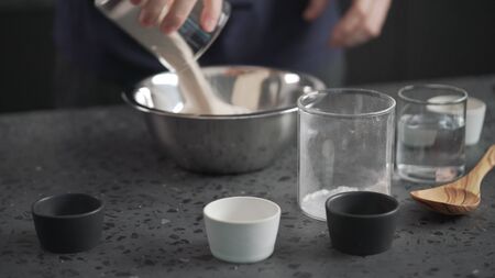 man adds dry ingredients into flour in steel bowl on concrete countertop, wide photo