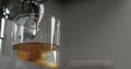 low angle pour from coffee machine into glass with waterの写真素材