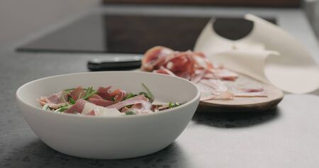 adding parmesan flakes to make salad with arugula, tomatoes and prosciuttoの写真素材