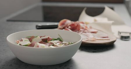pour olive oil over salad with prosciutto, cherry tomatoes and mixed salad leaves in white bowlの写真素材